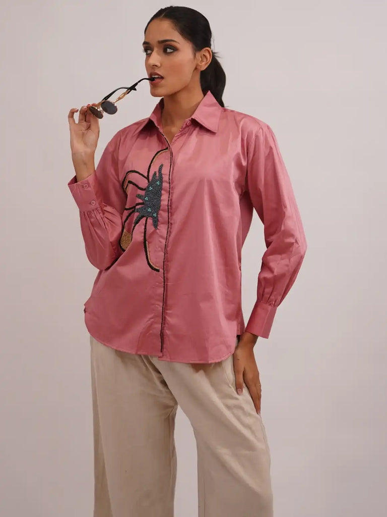 Woman wearing a pink shirt with a spider design and beige pants