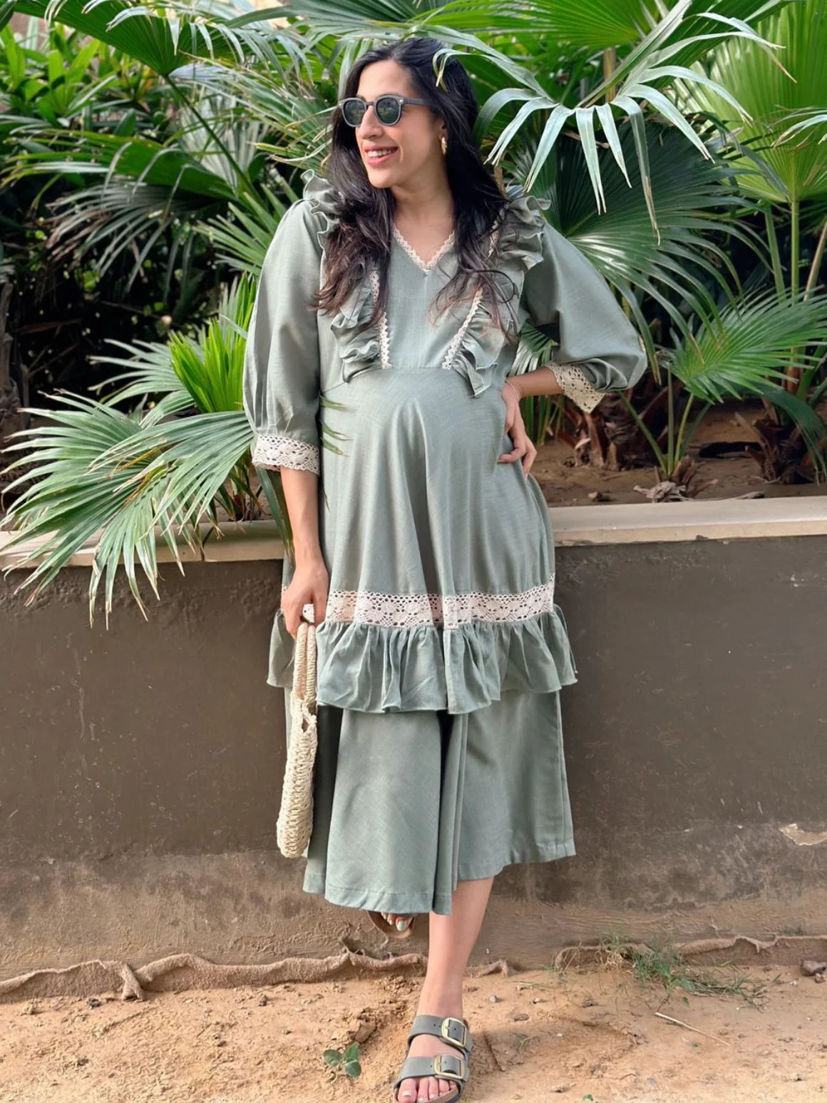 Woman in a green dress standing outdoors with plants in the background